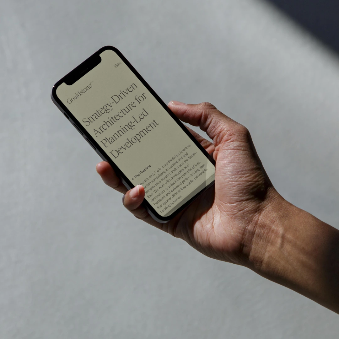A hand holding a mobile phone viewing the 'about us' page of the gouldstone website